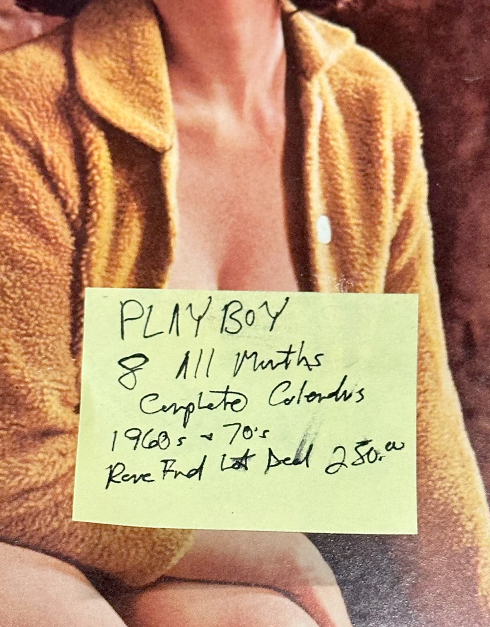 Person wearing a brown jacket with a handwritten note on a yellow sticky note, set against a blurred background.