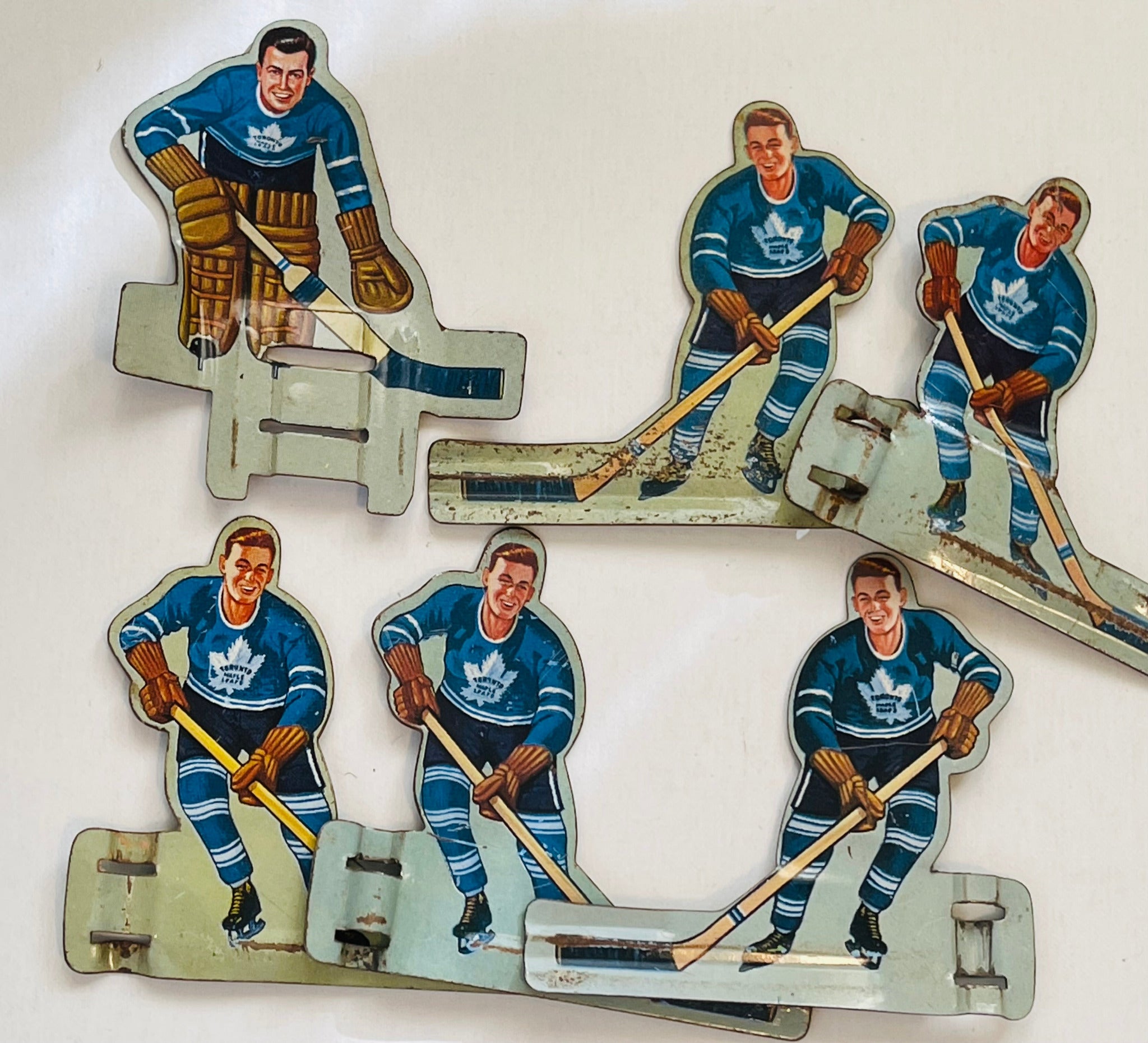 A set of six vintage metal hockey player figures from the 1960s, featuring the Toronto Maple Leafs team, with their sticks and uniforms visible.